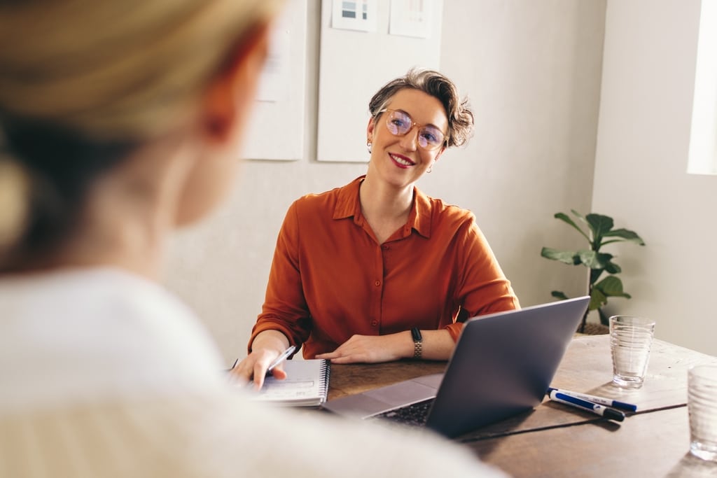 Happy hiring manager smiling while interviewing a job candidate in her office. Cheerful businesswoman having a meeting with a shortlisted job applicant in a creative workplace.